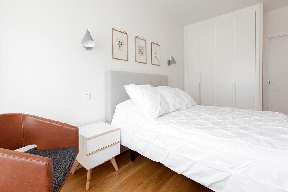 Proyecto de R de Room Amazing Homes. Dormitorio principal de diseño nórdico con cabecero tapizado en gris, mesillas de noche blancas y tocador de madera maciza.