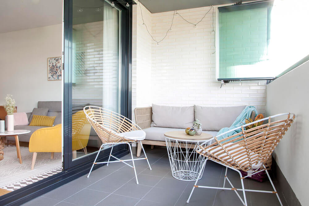 Proyecto de R de Room Amazing Homes. Terraza con sofá de madera maciza de acacia y cojines tapizados en gris y butacas de ratán y metal lacado en blanco.