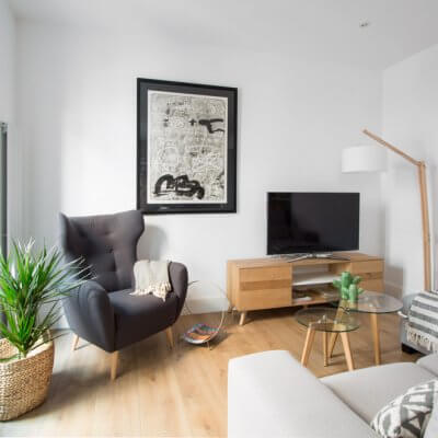 RdeRoom-MADERA reforma e interiorismo de vivienda para alquiler de lujo en Malasaña. Estar con orejero, sofá gris y mueble TV madera