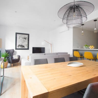 RdeRoom-MADERA reforma e interiorismo de vivienda para alquiler de lujo en Malasaña. Estar-comedor con cocina integrada. Mesa de madera. Taburetes tapizados.