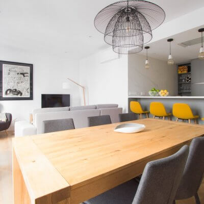 RdeRoom-MADERA reforma e interiorismo de vivienda para alquiler de lujo en Malasaña. Estar-comedor con cocina integrada. Mesa de madera. Taburetes tapizados.
