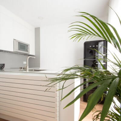 Proyecto de reforma de vivienda en Chamberí II (Madrid) de R de Room. Cocina abierta con península y frigorífico SMEG en color negro. Pared de ladrillo visto original. Radiador Runtal.
