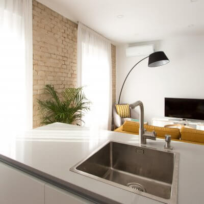 Proyecto de reforma de vivienda en Chamberí II (Madrid) de R de Room. Cocina abierta con península. Sofá modelo MAD en color mostaza de estilo mid-century. Lámpara de pie con forma de arco en color negro.