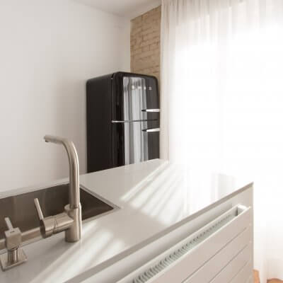 Proyecto de reforma de vivienda en Chamberí II (Madrid) de R de Room. Cocina abierta con península y frigorífico SMEG en color negro. Pared de ladrillo visto original. Radiador Runtal.