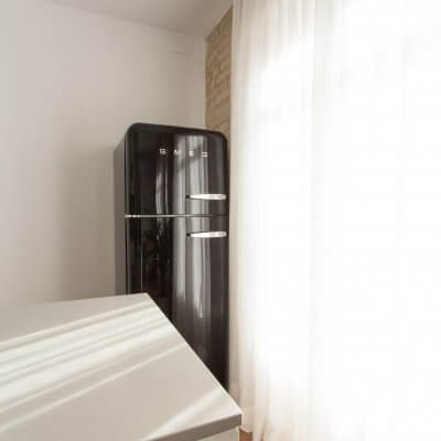 Proyecto de reforma de vivienda en Chamberí II (Madrid) de R de Room. Cocina abierta con península y frigorífico SMEG en color negro. Pared de ladrillo visto original. Radiador Runtal.
