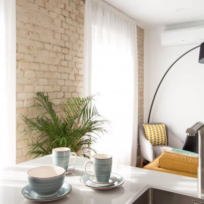 Proyecto de reforma de vivienda en Chamberí II (Madrid) de R de Room. Cocina abierta al salón con península. Muebles blancos y encimera de Silestone en color gris claro. Pared de ladrillo visto original.
