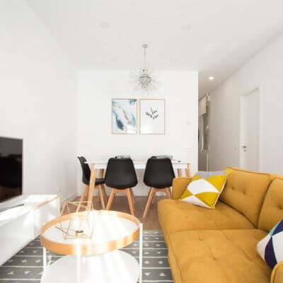 Proyecto de reforma de vivienda en Chamberí II (Madrid) de R de Room. Estar-comedor de estilo escandinavo. Lámpara de techo Sputnik resturada. Sofá modelo MAD en color mostaza y muebles de diseño nórdico en blanco y madera. Láminas de gran formado de Desenio.