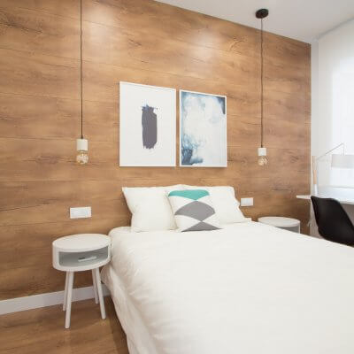 Proyecto de reforma de vivienda en Chamberí II (Madrid) de R de Room. Dormitorio principal con suelo laminado de madera y pared del cabecero forrada en laminado de madera. Lámparas colgantes de mármol blanco bombilla Edison. Mesita de noche modelo BLOCK en color blanco. Zona de escritorio.