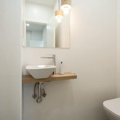 Proyecto de reforma de vivienda en Chamberí II (Madrid) de R de Room. Aseo con lámpara de techo colgante. Casquillo de madera con bombilla EDISON. Encimera a medida con lavabo sobre encimera de dimensiones reducidas.