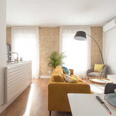 Proyecto de reforma de vivienda en Chamberí II (Madrid) de R de Room. Estar-comedor de estilo escandinavo. Lámpara de techo Sputnik resturada. Sofá modelo MAD en color mostaza y muebles de diseño nórdico en blanco y madera. Láminas de gran formado de Desenio.