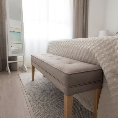 El banco de pie de cama tapizado en gris (a juego con el cabecero) sirve como descalzadora y para dejar los cojines por la noche. El espejo con puerta es perfecto para tener todos los complementos ordenados.