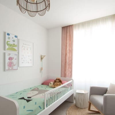 La decoración se plantea en tonos neutros (como la cama nido blanca o la mecedera gris), con toques naturales (en la alfombra de yute y la lámpara de bambú), y una combinación de dos colores, verde y rosa, en los textiles.