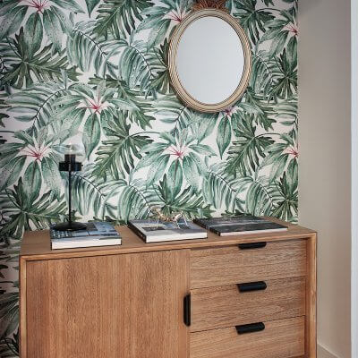 Recibidor de vivienda en Madrid. Papel pintado con estampado tropical, espejo piña dorado y mueble de estilo midcentury con tiradores negros. Proyecto de reforma e interiorismo de R de Room.