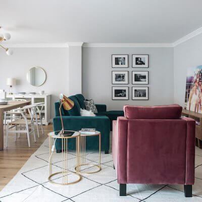 Salón y comedor de vivienda en Madrid. Proyecto de reforma e interiorismo de R de Room. Sofá tapizado en terciopelo verde y butaca tapizada en terciopelo rosa. Mesillas auxiliares doradas y alfombra tipo Beni Ouarain, blanca con rombos negros. Mesa de madera y lámpara suspendida dorada. Collage de cuadros. Proyecto de reforma e interiorismo de R de Room.