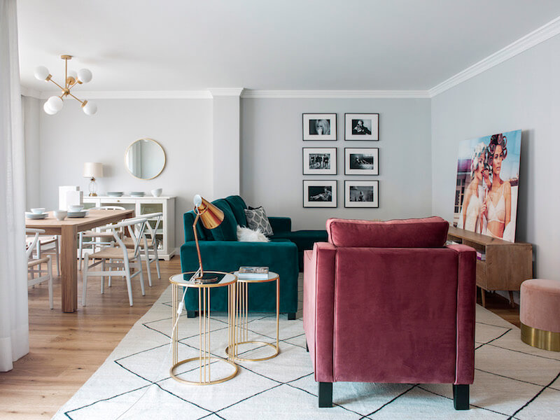 Salón y comedor de vivienda en Madrid. Proyecto de reforma e interiorismo de R de Room. Sofá tapizado en terciopelo verde y butaca tapizada en terciopelo rosa. Mesillas auxiliares doradas y alfombra tipo Beni Ouarain, blanca con rombos negros. Mesa de madera y lámpara suspendida dorada. Collage de cuadros. Proyecto de reforma e interiorismo de R de Room.