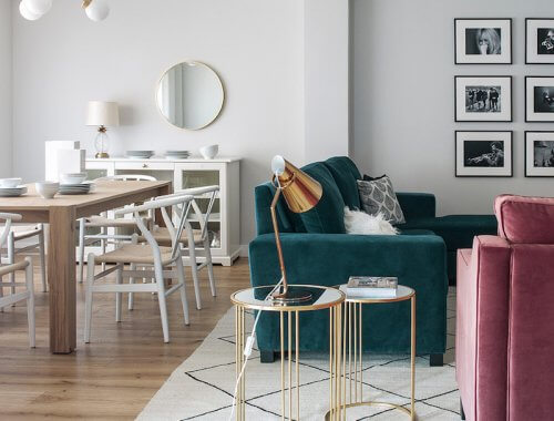 Salón y comedor de vivienda en Madrid. Proyecto de reforma e interiorismo de R de Room. Sofá tapizado en terciopelo verde y butaca tapizada en terciopelo rosa. Mesillas auxiliares doradas y alfombra tipo Beni Ouarain, blanca con rombos negros. Mesa de madera y lámpara suspendida dorada. Collage de cuadros.