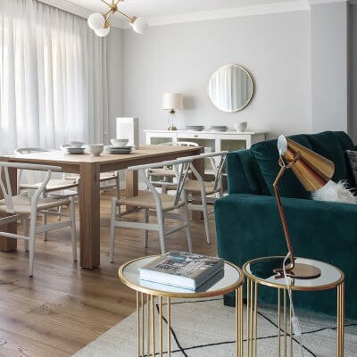Salón y comedor de vivienda en Madrid. Proyecto de reforma e interiorismo de R de Room. Sofá tapizado en terciopelo verde. Mesillas auxiliares doradas y alfombra tipo Beni Ouarain, blanca con rombos negros. Mesa rectangular de madera de roble extensible y lámpara suspendida dorada. Salón contemporáneo, luminoso y acogedor. Proyecto de reforma e interiorismo de R de Room.