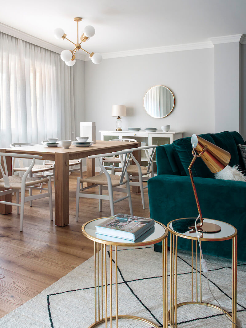 Salón y comedor de vivienda en Madrid. Proyecto de reforma e interiorismo de R de Room. Sofá tapizado en terciopelo verde. Mesillas auxiliares doradas y alfombra tipo Beni Ouarain, blanca con rombos negros. Mesa rectangular de madera de roble extensible y lámpara suspendida dorada. Salón contemporáneo, luminoso y acogedor. Proyecto de reforma e interiorismo de R de Room.