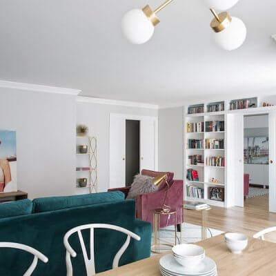 Salón y comedor de vivienda en Madrid. Mesa rectangular de madera de roble extensible. Sillas CH24 blancas. Lámpara suspendida dorada. Comedor contemporáneo, luminoso y acogedor. Salón con sofá de terciopelo verde y butaca de terciopelo rosa. Librería a medida con puerta corredera doble integrada. Proyecto de reforma e interiorismo de R de Room.