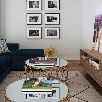Salón de vivienda en Madrid. Sofá de terciopelo verde. Mesas de centro doradas. Alfombra tipo Beni Ouarain de fondo blanco y rombos negros. Collage de fotografías en blanco y negro.