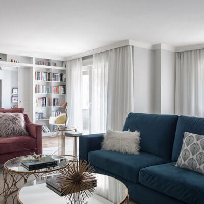 Salón de vivienda en Madrid. Zona de estar con sofá de terciopelo verde y butaca de terciopelo rosa. Librería a medida con puerta corredera doble integrada. Mesas de centro doradas. Proyecto de reforma e interiorismo de R de Room.