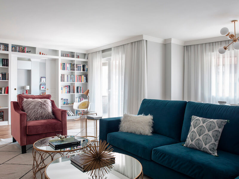 Salón de vivienda en Madrid. Zona de estar con sofá de terciopelo verde y butaca de terciopelo rosa. Librería a medida con puerta corredera doble integrada. Mesas de centro doradas. Proyecto de reforma e interiorismo de R de Room.