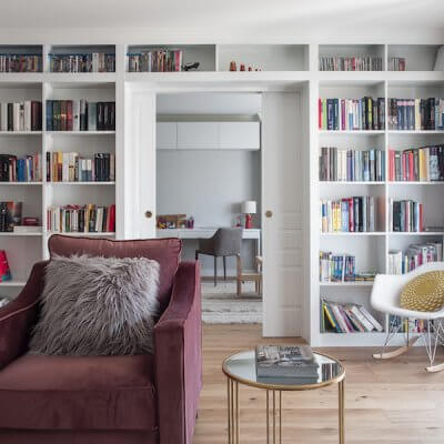 Salón de vivienda en Madrid. Zona de estar con butaca de terciopelo rosa. Librería a medida con puerta corredera doble integrada. Mesas auxiliares doradas. Proyecto de reforma e interiorismo de R de Room.