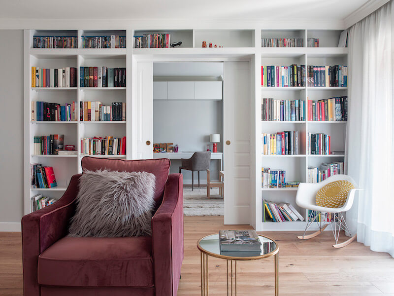 Salón de vivienda en Madrid. Zona de estar con butaca de terciopelo rosa. Librería a medida con puerta corredera doble integrada. Mesas auxiliares doradas. Proyecto de reforma e interiorismo de R de Room.