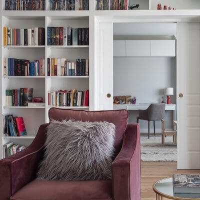 Salón de vivienda en Madrid. Zona de estar con butaca de terciopelo rosa. Librería a medida con puerta corredera doble integrada. Mesas auxiliares doradas. Proyecto de reforma e interiorismo de R de Room.