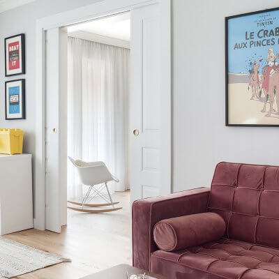 Salón de vivienda en Madrid. Espacios conectados a través de puertas correderas. Sofá de terciopelo rosa con capitoné. Cuarto infantil y zona de juegos. Mecedora Rocking Chair de Charles Eames. Proyecto de reforma e interiorismo de R de Room.