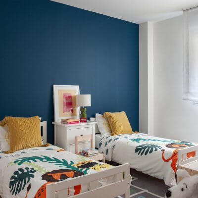 Dormitorio infantil de vivienda en Madrid. Pared del cabecero pintada en color azul pato. Colchas con estampado de animales y cojines mostaza. Cuarto de niños. Proyecto de reforma e interiorismo de R de Room.