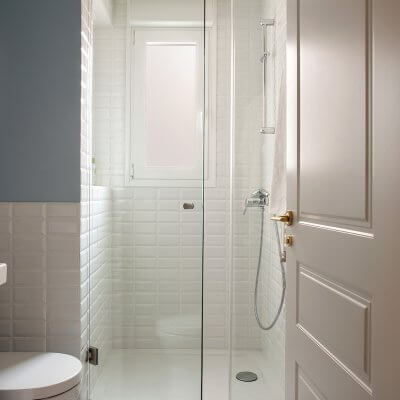 Baño con ducha en Madrid. Zócalo de azulejo metro blanco y pared pintada en color azul. Baldosa con estampado blanco y azul. Puerta blanca plafonada con tiradores dorados. Mueble de baño Hemnes de IKEA. Proyecto de reforma e interiorismo de R de Room.