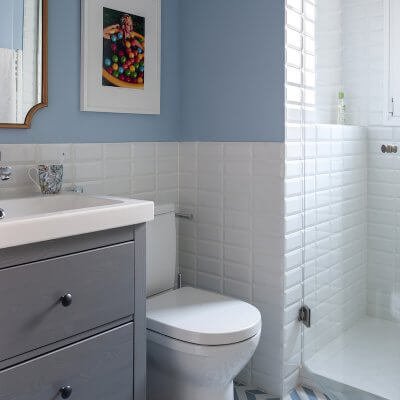Baño con ducha en Madrid. Zócalo de azulejo metro blanco y pared pintada en color azul. Baldosa con estampado blanco y azul. Puerta blanca plafonada con tiradores dorados. Mueble de baño Hemnes de IKEA. Proyecto de reforma e interiorismo de R de Room.