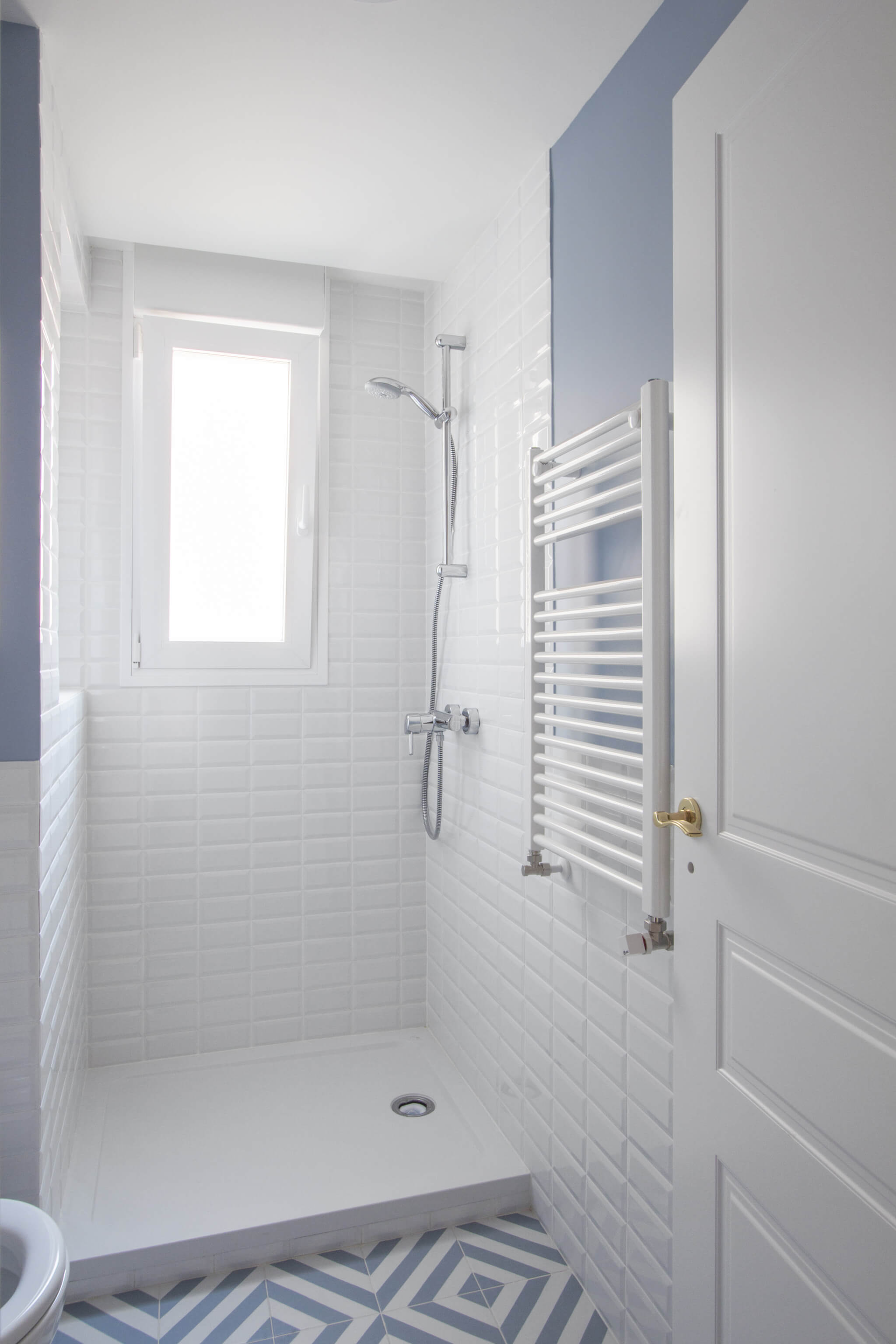 Baño con ducha en Madrid. Zócalo de azulejo metro blanco y pared pintada en color azul. Baldosa con estampado blanco y azul. Puerta blanca plafonada con tiradores dorados. Mueble de baño Hemnes de IKEA. Proyecto de reforma e interiorismo de R de Room.