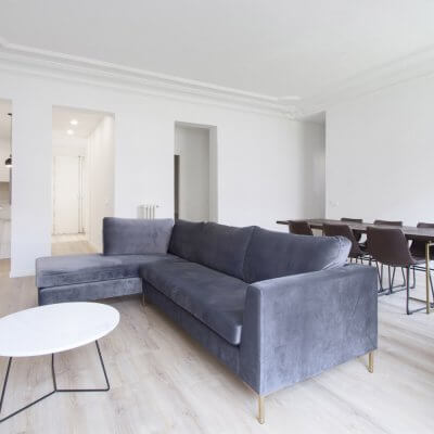 Proyecto de reforma en Chamberí (Madrid) de R de Room. Salón minimalista con cocina abierta. Molduras. Sofá gris. Espejo dorado.