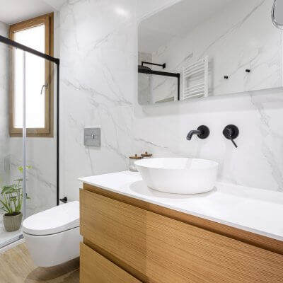 Elegante baño con mármol en las paredes y azulejo porcelánico efecto madera en el suelo combinado con mueble de madera. Proyecto de R de Room.
