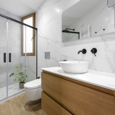 Elegante baño con mármol en las paredes y azulejo porcelánico efecto madera en el suelo combinado con mueble de madera. Proyecto de R de Room.