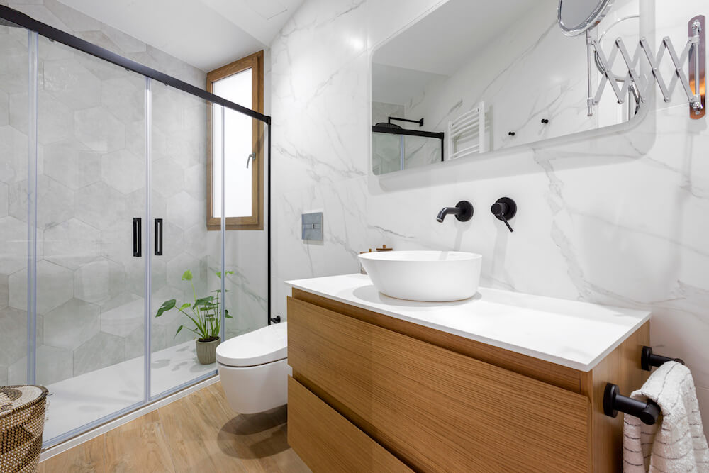 Elegante baño con mármol en las paredes y azulejo porcelánico efecto madera en el suelo combinado con mueble de madera. Proyecto de R de Room.