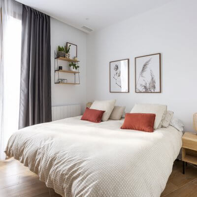 Dormitorio principal sencillo y acogedor donde los toques de madera de las mesitas y la estantería son los protagonistas. Proyecto de R de Room.