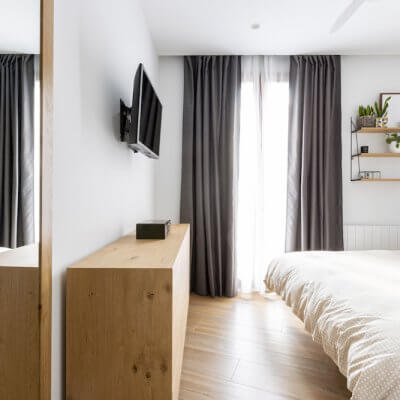 Dormitorio principal sencillo y acogedor donde los toques de madera de las mesitas, la cómoda y la estantería son los protagonistas. Proyecto de R de Room.