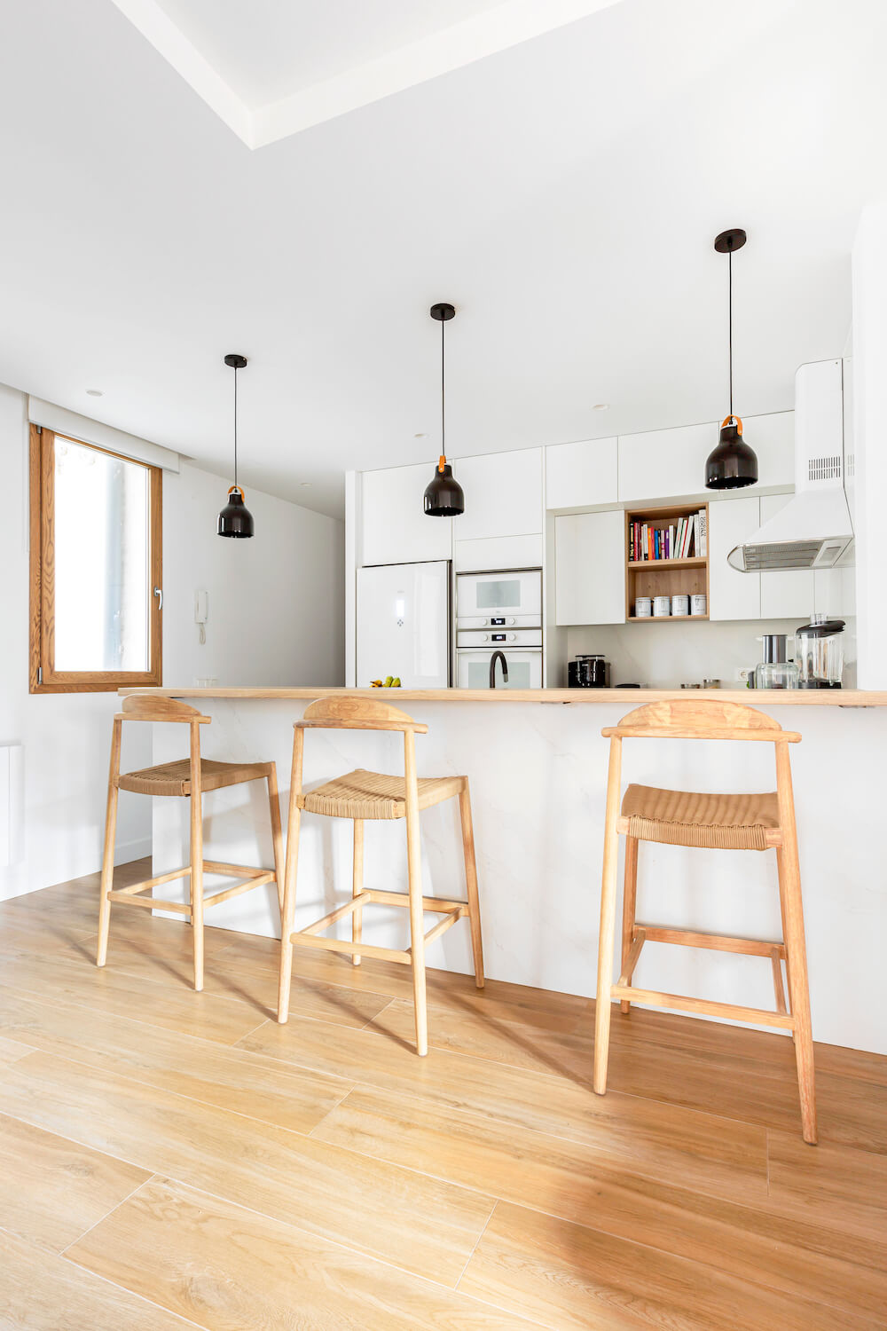 Barra en cocina abierta. Predomina el blanco con toques de madera. La encimera y los taburetes son el toque cálido perfecto para esta casa. Proyecto de R de Room.