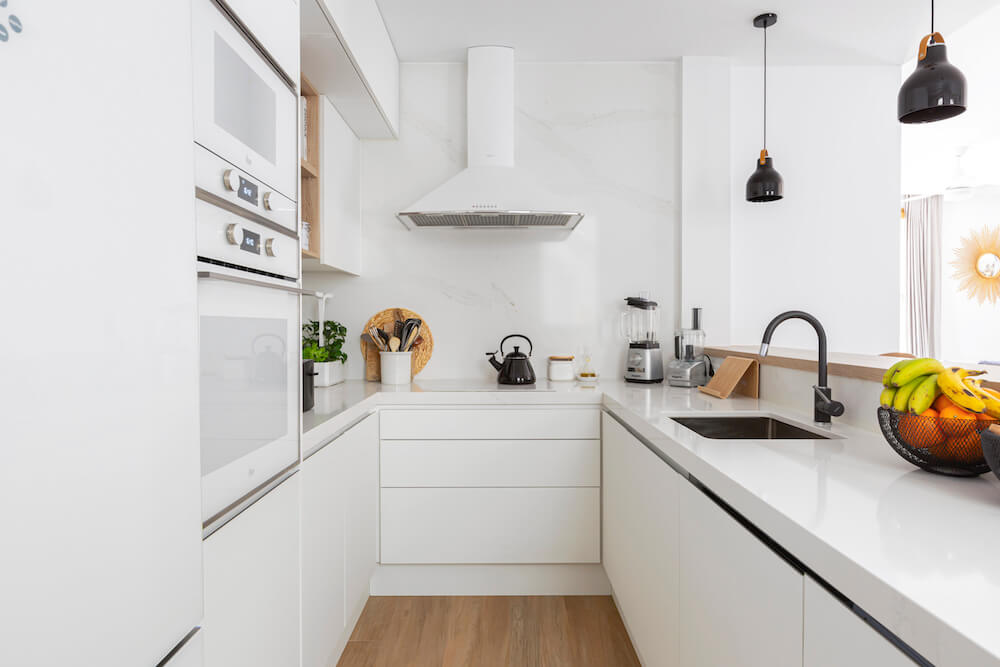 Cocina blanca con península abierta al salón. Detalles negros en grifo, lámparas y decoración. Proyecto de R de Room.