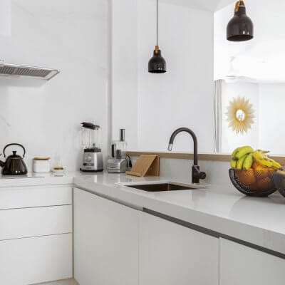 Cocina blanca con península abierta al salón. Detalles negros en grifo, lámparas y decoración. Proyecto de R de Room.