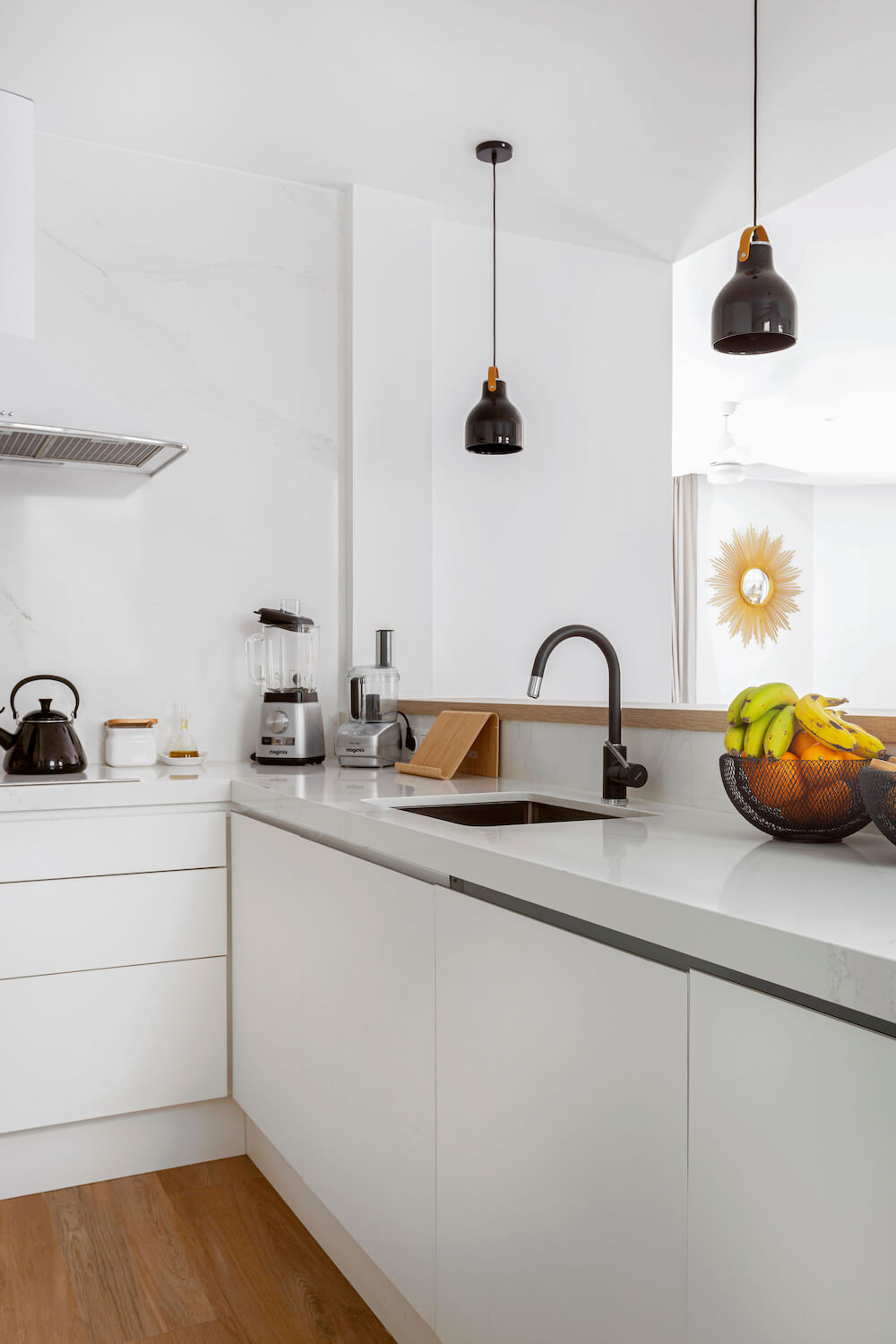 Cocina blanca con península abierta al salón. Detalles negros en grifo, lámparas y decoración. Proyecto de R de Room.