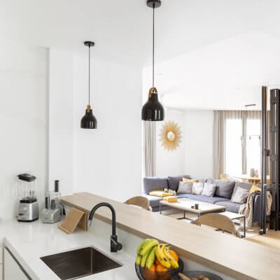 Cocina blanca con península abierta al salón. Detalles negros en grifo, lámparas y decoración. Proyecto de R de Room.