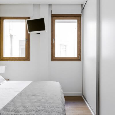 Sencillo pero efectivo dormitorio para invitados. Mesitas de madera, ropa de cama neutra y pared pintada en amarillo. Proyecto de R de Room.