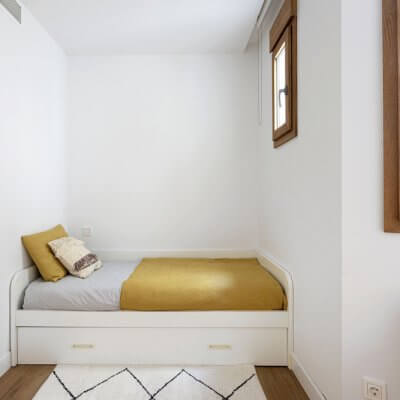 Dormitorio para invitados con cama nido y sillón Acapulco de ratán. Detalle con alfombra bereber. Proyecto de R de Room.